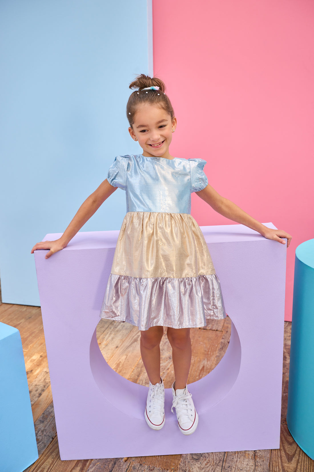 Tween model can be seen wearing a metallic dress that has an ice blue metallic top, gold metallic waist, and purple metallic bottom tier for a fun elevated look. 