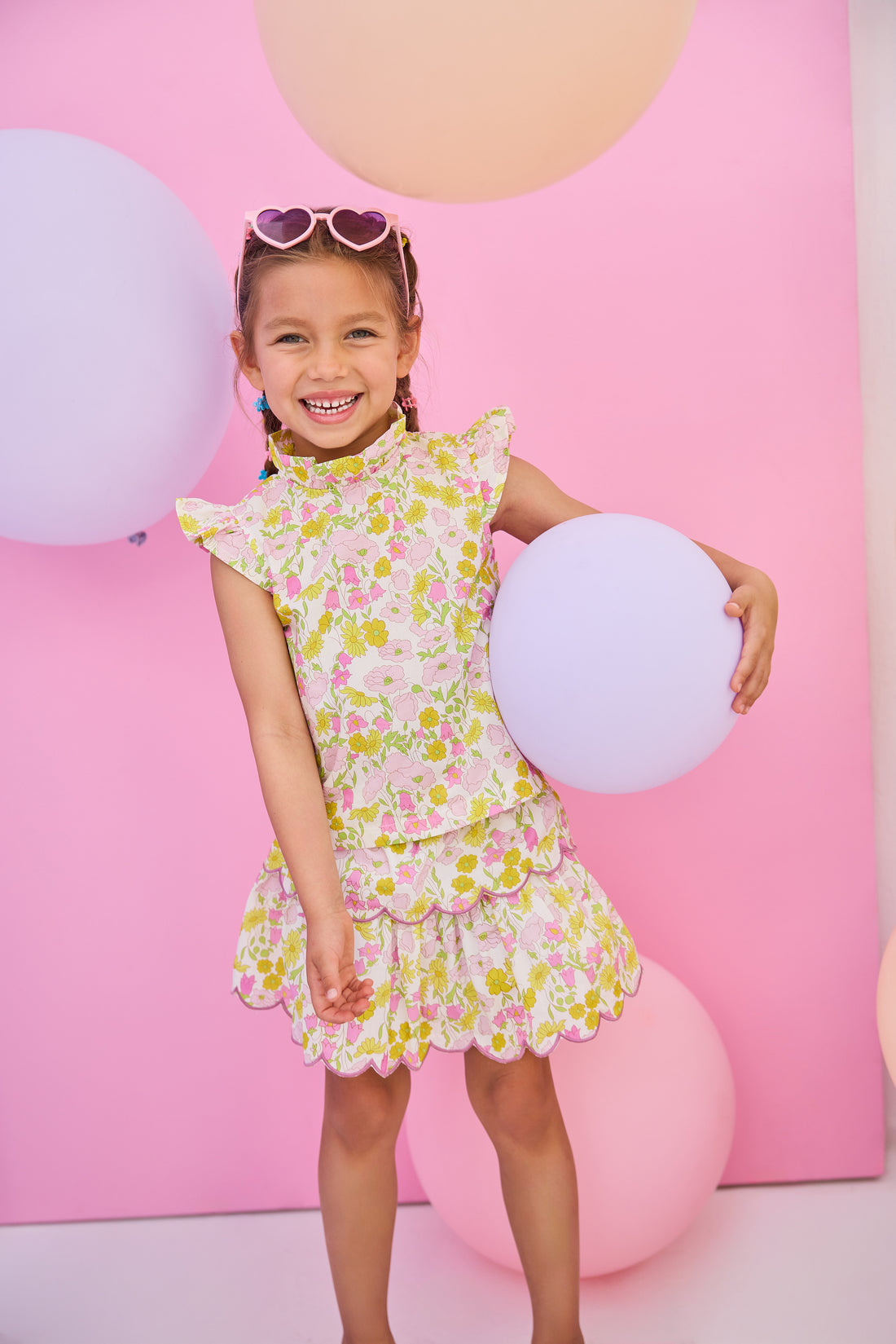 Model can be seen wearing woven two tiered skort in a pink/yellow floral print. Skort features built in shorts, elastic waistband, and a cream scallop embroidery detailing to complete the look. Skort pairs back perfectly with woven top in the same print to complete the look. 