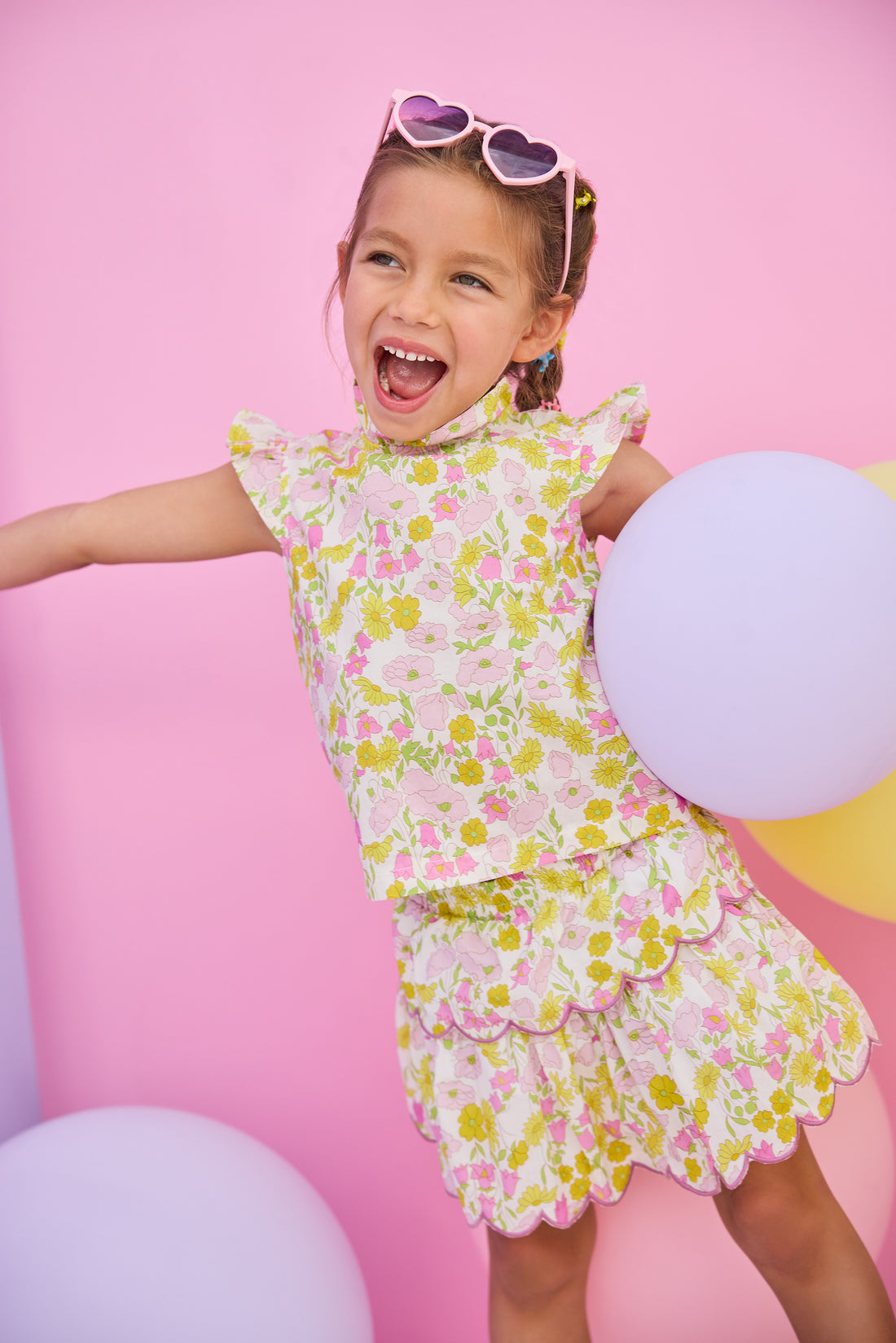 Model can be seen wearing woven two tiered skort in a pink/yellow floral print. Skort features built in shorts, elastic waistband, and a cream scallop embroidery detailing to complete the look. Skort pairs back perfectly with woven top in the same print to complete the look. 