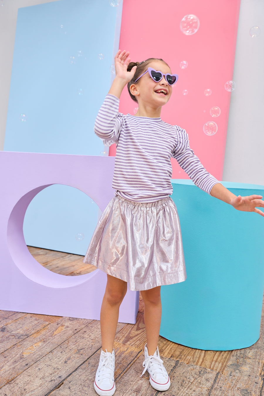 Young girl in a striped shirt and shiny skirt posing in front of colorful geometric shapes.