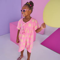 Model can be seen wearing a knit terry material dress in bubblegum pink with yellow flowers. Dress features v-neckline with tassel ties to elevate the look. 