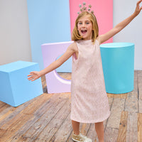 Young girl in a pink crinkle dress with gold stars holding a disco ball in a colorful room.