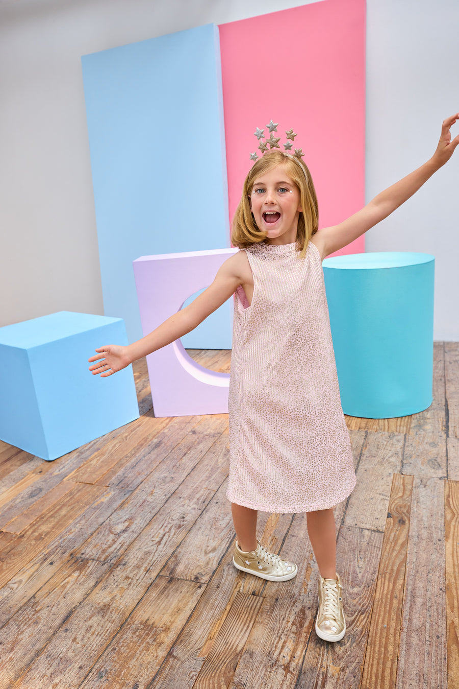 Young girl in a pink crinkle dress with gold stars holding a disco ball in a colorful room.