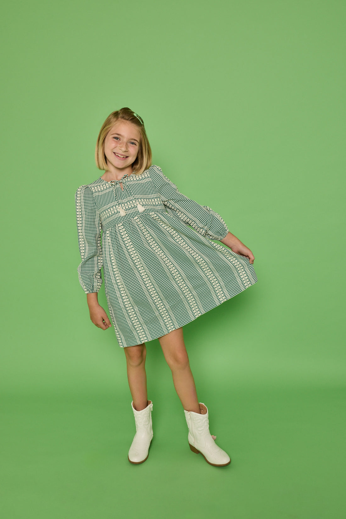 Model can be seen wearing a long sleeve woven seersucker dress in a green and cream pattern. Dress features tie with tassels at v-neckline for an elevated look.