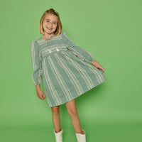 Model can be seen wearing a long sleeve woven seersucker dress in a green and cream pattern. Dress features tie with tassels at v-neckline for an elevated look.