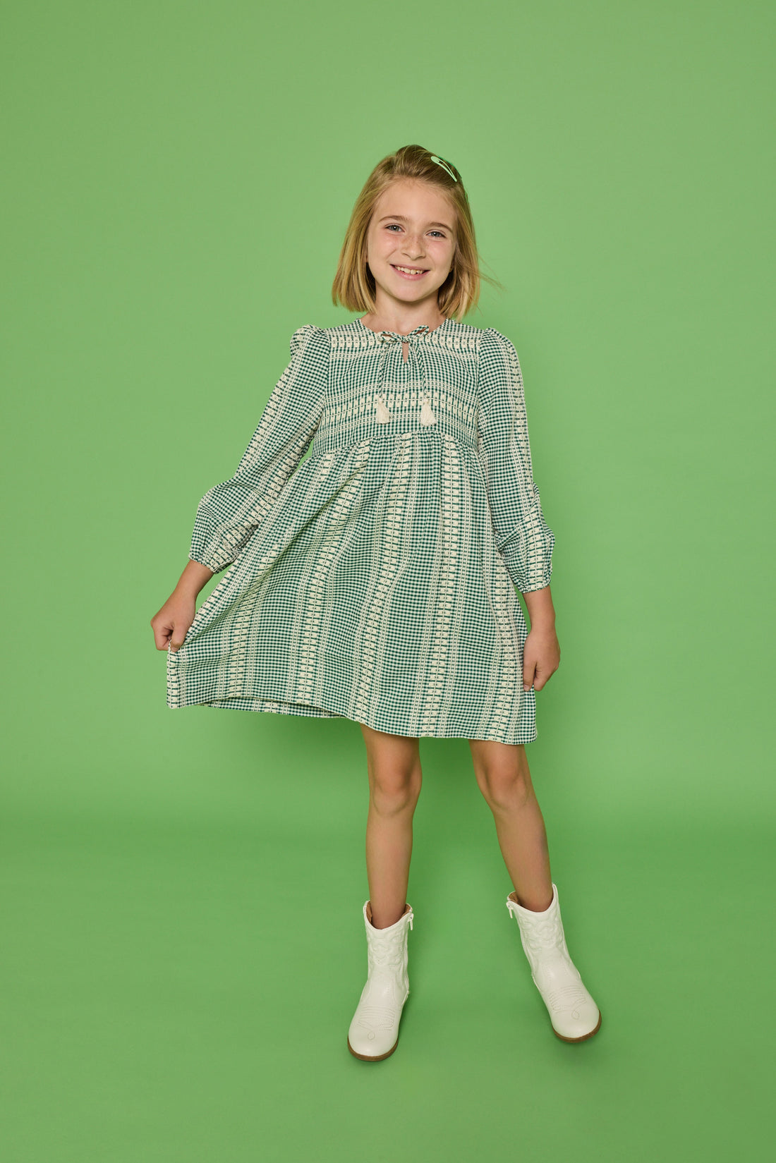 Model can be seen wearing a long sleeve woven seersucker dress in a green and cream pattern. Dress features tie with tassels at v-neckline for an elevated look.