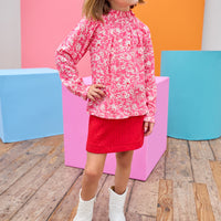 Model can be seen wearing rayon long sleeve top in a hot pink/red/white floral paired back with a quilted red skort to complete the look. Top has high collar, with elastic neckline, for a stretchy but form fitting fit. 