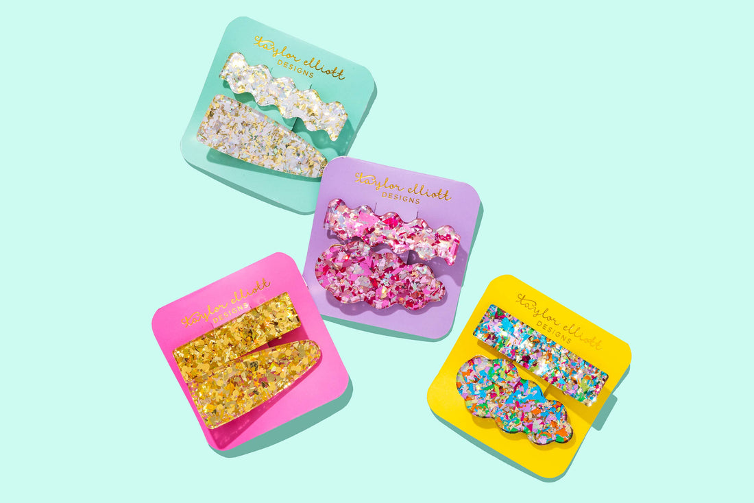 Set of colorful floral hair clips in branded cases on a light blue background