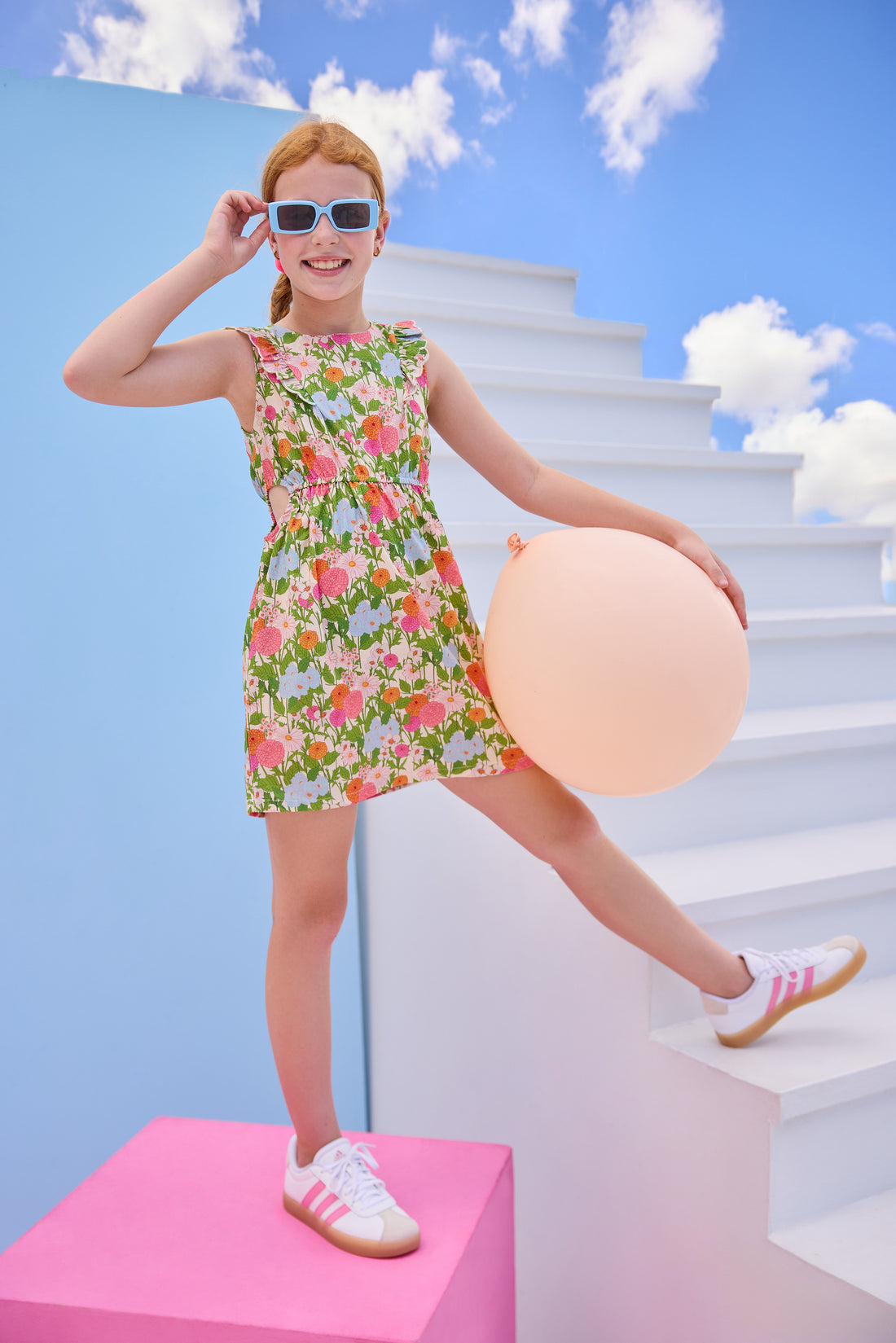 Model can be seen wearing a woven green/pink/orange/light blue floral dress that features two cutout features on the sides of the dress to give it an elevated/big girl feel. 