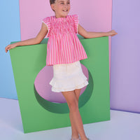 Model can be seen wearing a red/pink/white stripe woven top that features a square neckline and white pom pom trim along the sleeves to elevate the look. 
