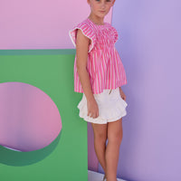Model can be seen wearing a red/pink/white stripe woven top that features a square neckline and white pom pom trim along the sleeves to elevate the look. 