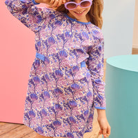 Model can be seen wearing woven dress in blue/purple/white floral print that features velour royal blue detailing along neckline and cuffs of sleeves and also has button closure down center of neck for secure but comfy fit. 