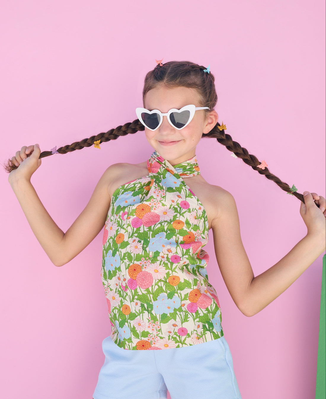tween girl in a floral top and light blue shorts posing against a colorful background