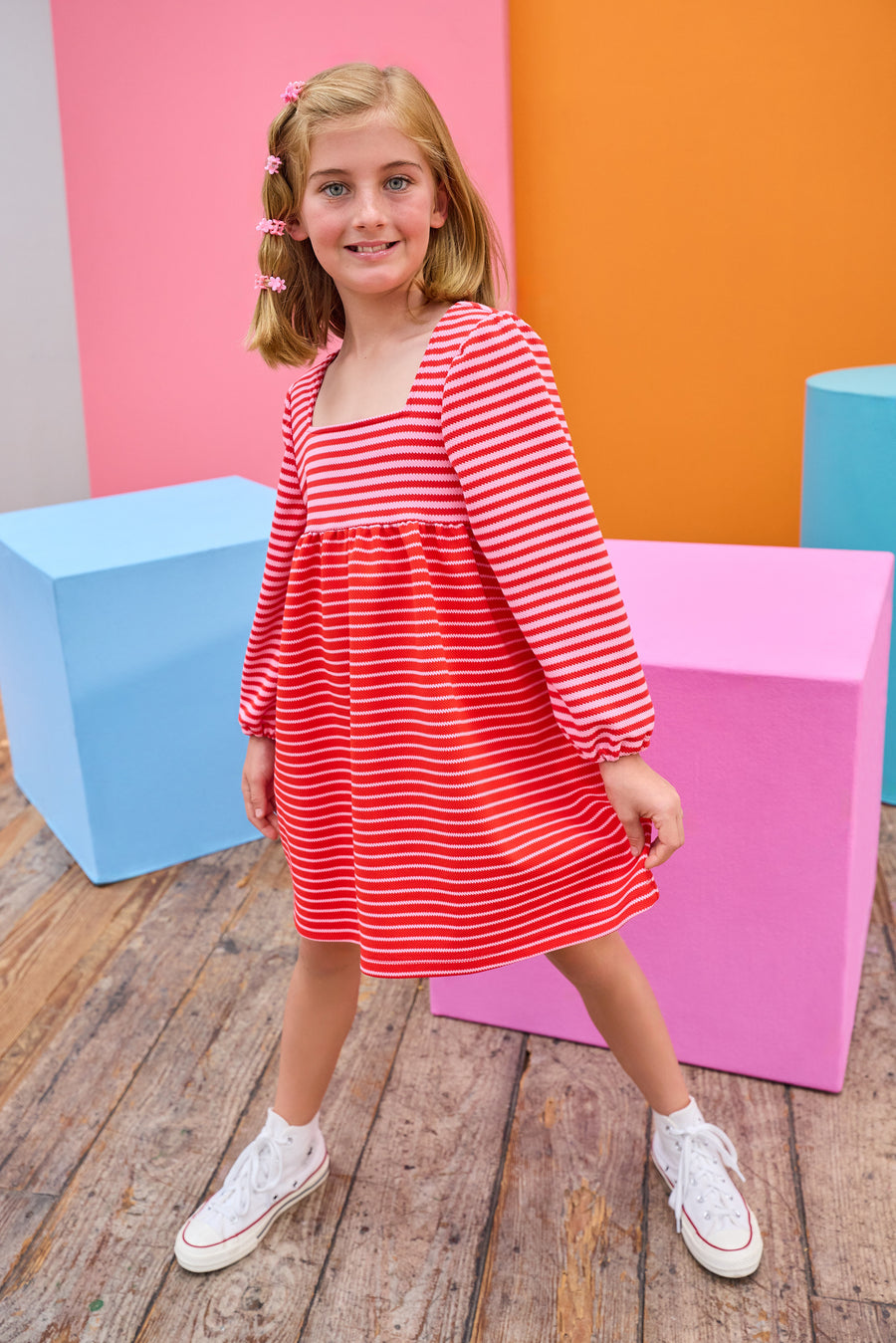 Model can be seen wearing a thick knit long sleeve dress that features a square neckline, elastic cuffs at sleeve, and a mix and match pink and red stripe detail to elevate the look.