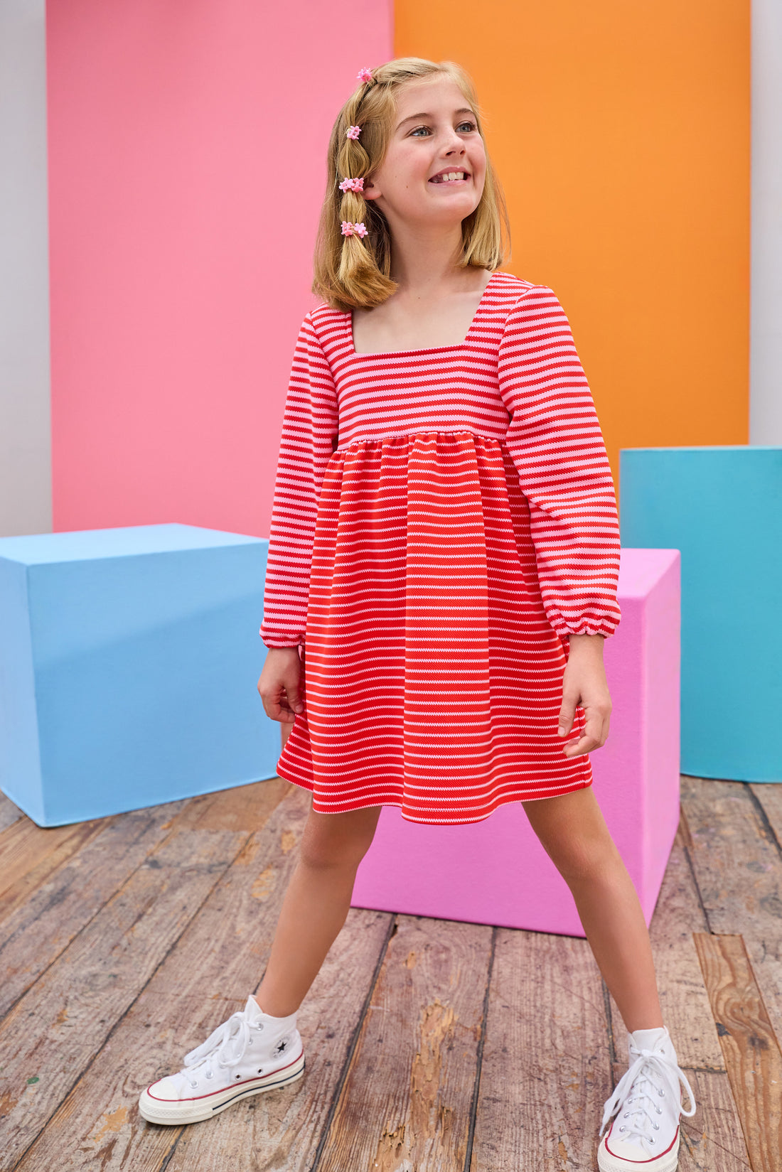 Model can be seen wearing a thick knit long sleeve dress that features a square neckline, elastic cuffs at sleeve, and a mix and match pink and red stripe detail to elevate the look.