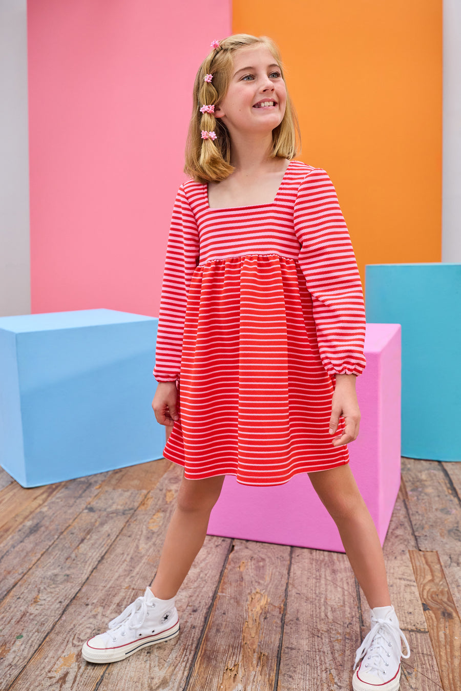 Model can be seen wearing a thick knit long sleeve dress that features a square neckline, elastic cuffs at sleeve, and a mix and match pink and red stripe detail to elevate the look.