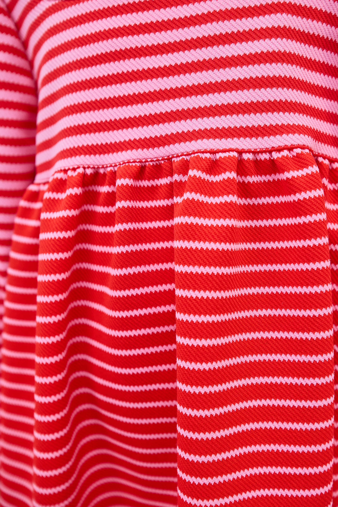 Model can be seen wearing a thick knit long sleeve dress that features a square neckline, elastic cuffs at sleeve, and a mix and match pink and red stripe detail to elevate the look.