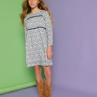 Model can be seen wearing a long sleeve woven dress in a blue/white floral print. Dress features two velour ribbon strips along bust and 3/4 quarter sleeves for an elevated look. 