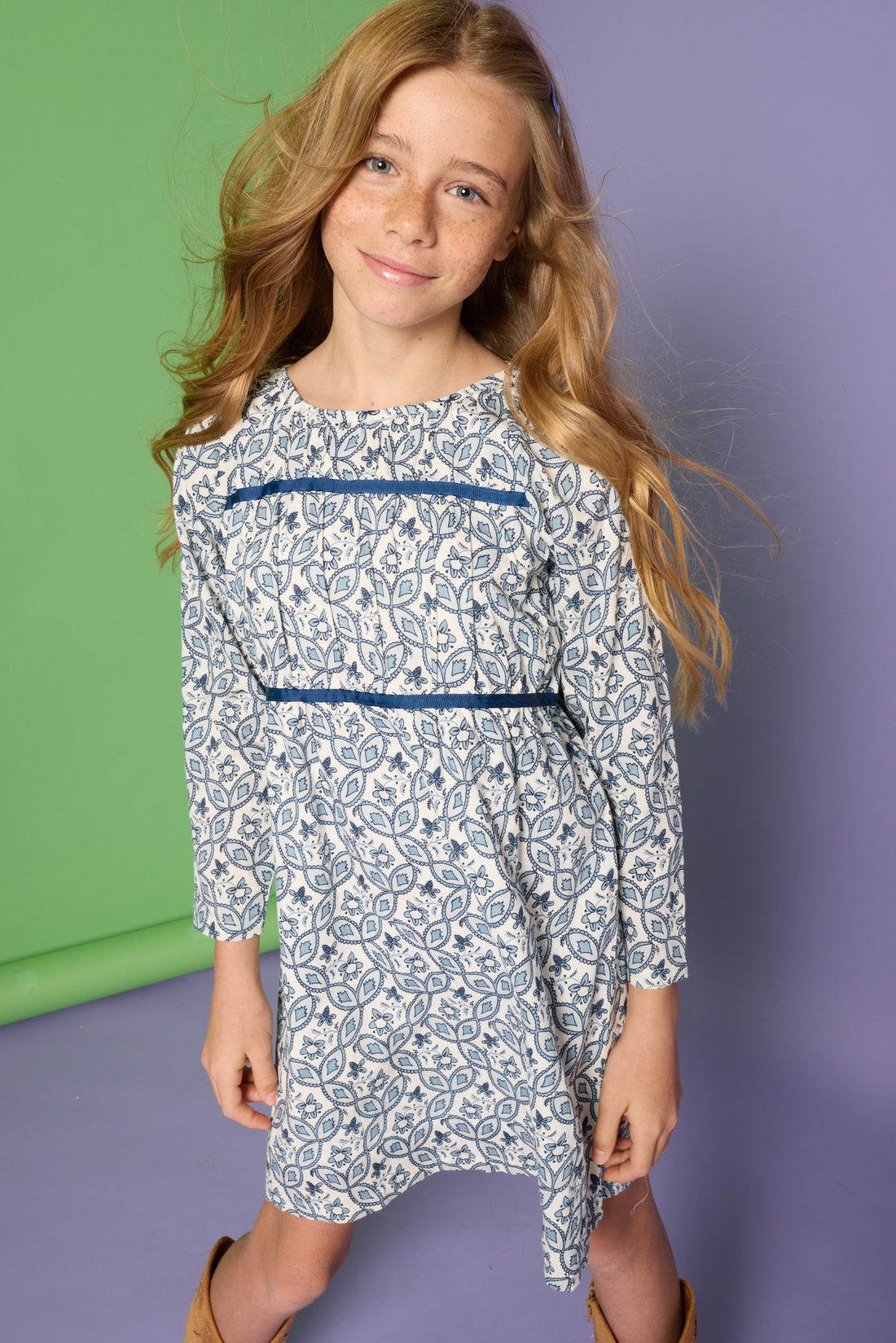 Model can be seen wearing a long sleeve woven dress in a blue/white floral print. Dress features two velour ribbon strips along bust and 3/4 quarter sleeves for an elevated look. 