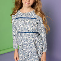 Model can be seen wearing a long sleeve woven dress in a blue/white floral print. Dress features two velour ribbon strips along bust and 3/4 quarter sleeves for an elevated look. 
