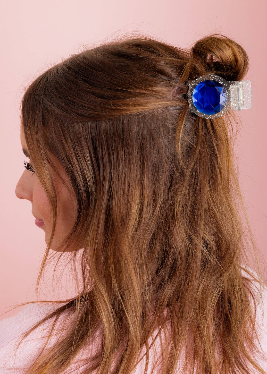 Woman with a hair bun featuring a decorative hair clip with a blue gem on a pink background