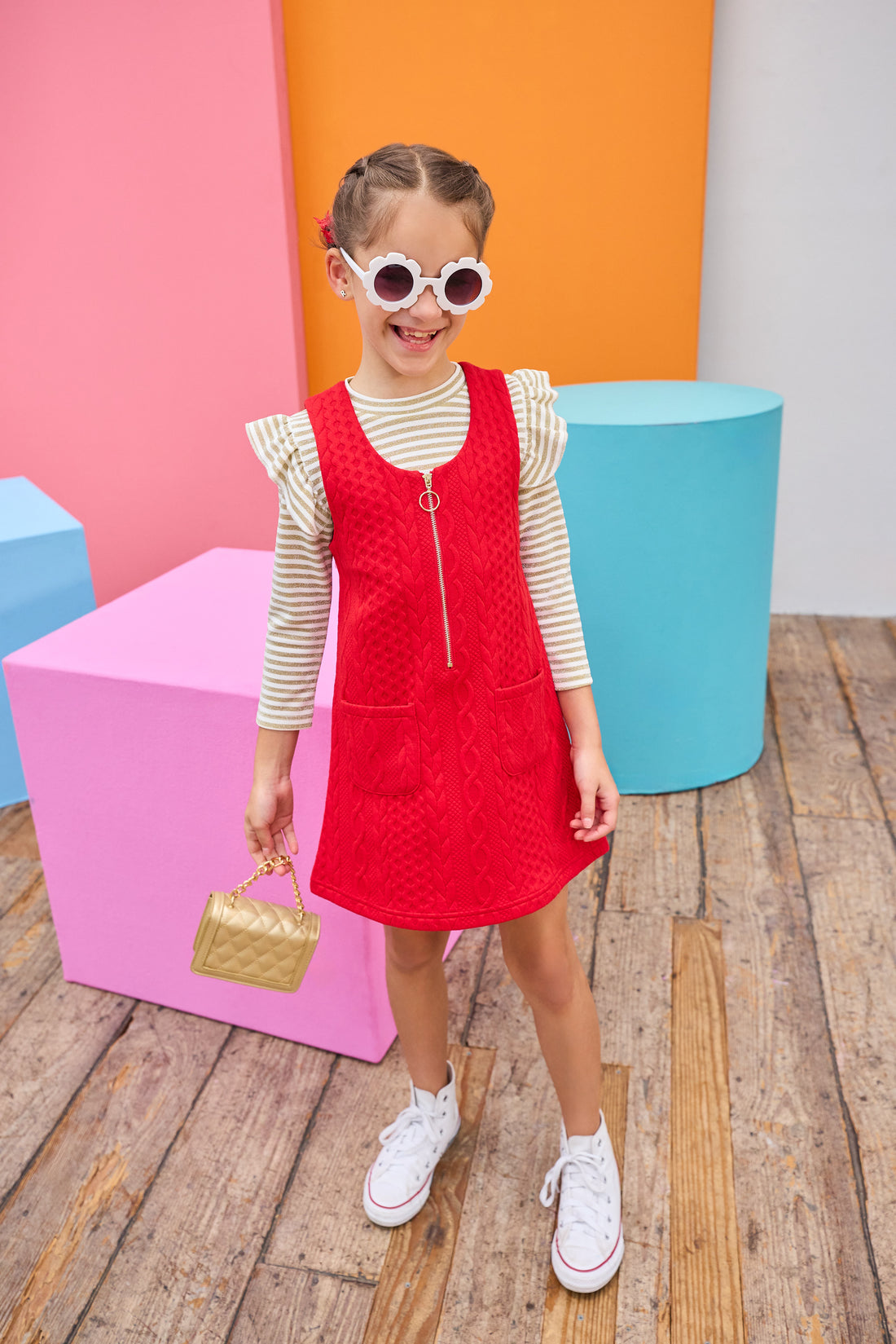 Young girl in a red dress with a gold striped top underneath with colorful geometric shapes in the background