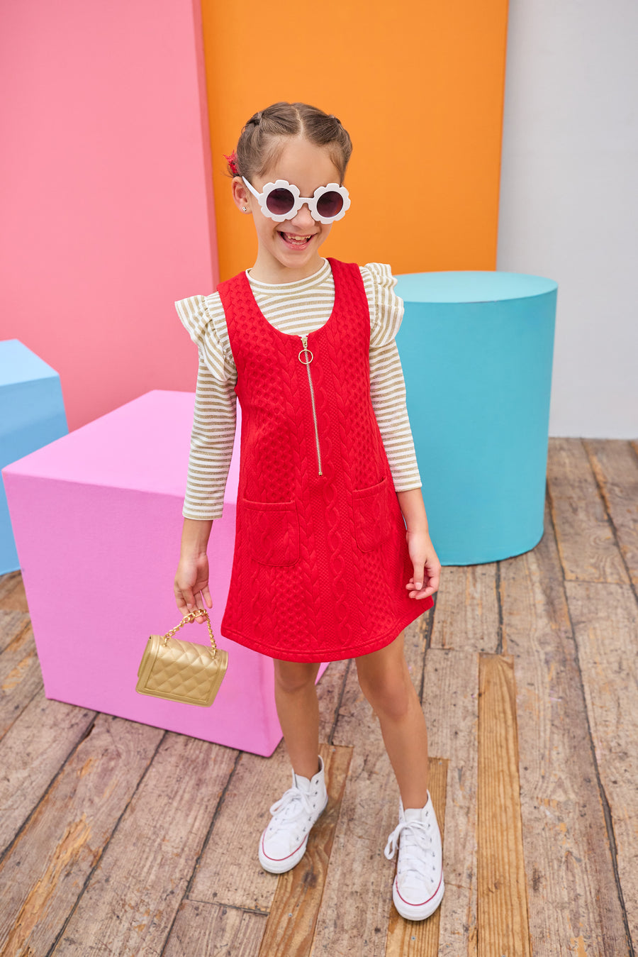 Young girl in a red dress with a gold striped top underneath with colorful geometric shapes in the background