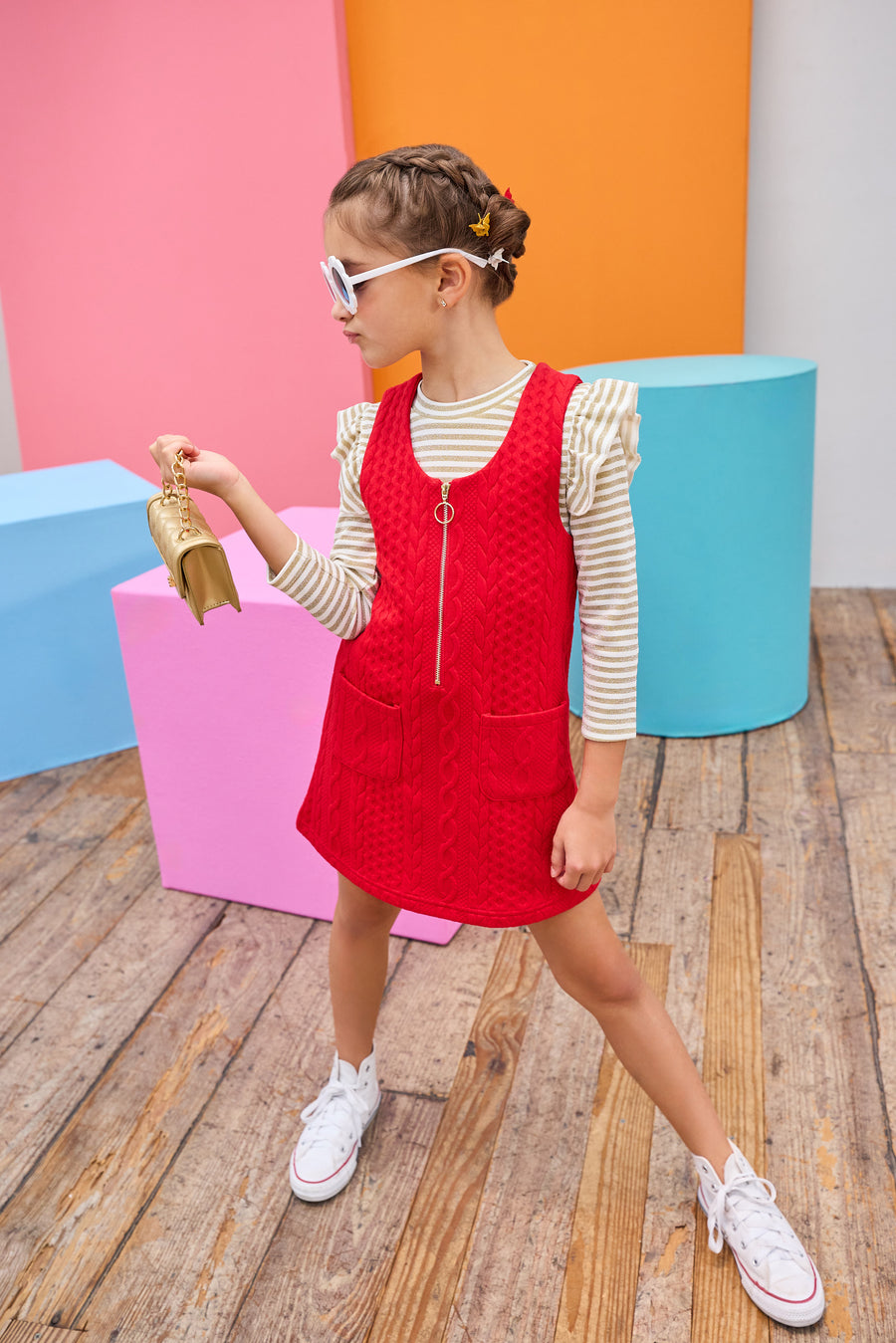 Young girl in a red dress standing in front of colorful geometric shapes on a wooden floor.