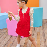 Model can be seen wearing a knit quilted jumper in a cherry red color that features a gold quarter zip zipper and  two functional pockets in the front for an elevated look. Paired back with  a long sleeve gold and white top underneath to complete the look. 