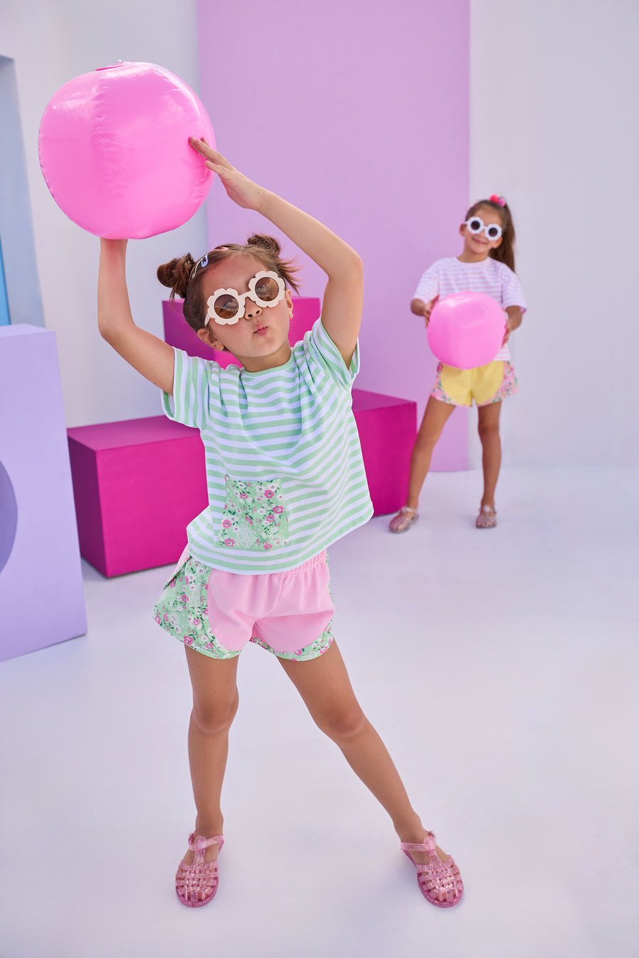 Girl/Tween basic pink athletic type track short with green/pink/white floral print along outside of shorts. Model can be seen pairing shorts back with the matching boxy tee that has the same print on a faux pocket square at bottom right of shirt. 