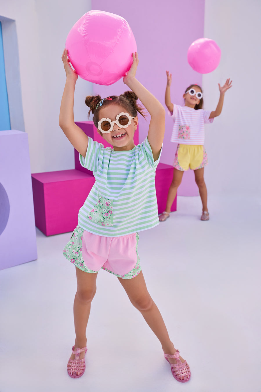 Girl/Tween basic pink athletic type track short with green/pink/white floral print along outside of shorts. Model can be seen pairing shorts back with the matching boxy tee that has the same print on a faux pocket square at bottom right of shirt. 