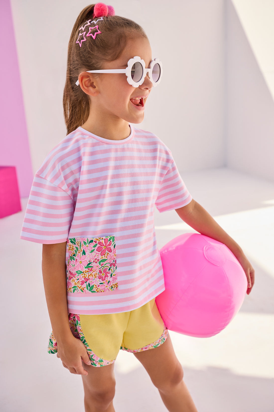 Girl/Tween model can be seen wearing a gorgeous pair of yellow knit athletic shorts that have a hot pink/yellow/green floral pattern on the trim of shorts. This floral pattern matches back perfectly with our knit pink and white stripe boxy tee that has the same floral detailing on the front faux pocket to complete the look. 