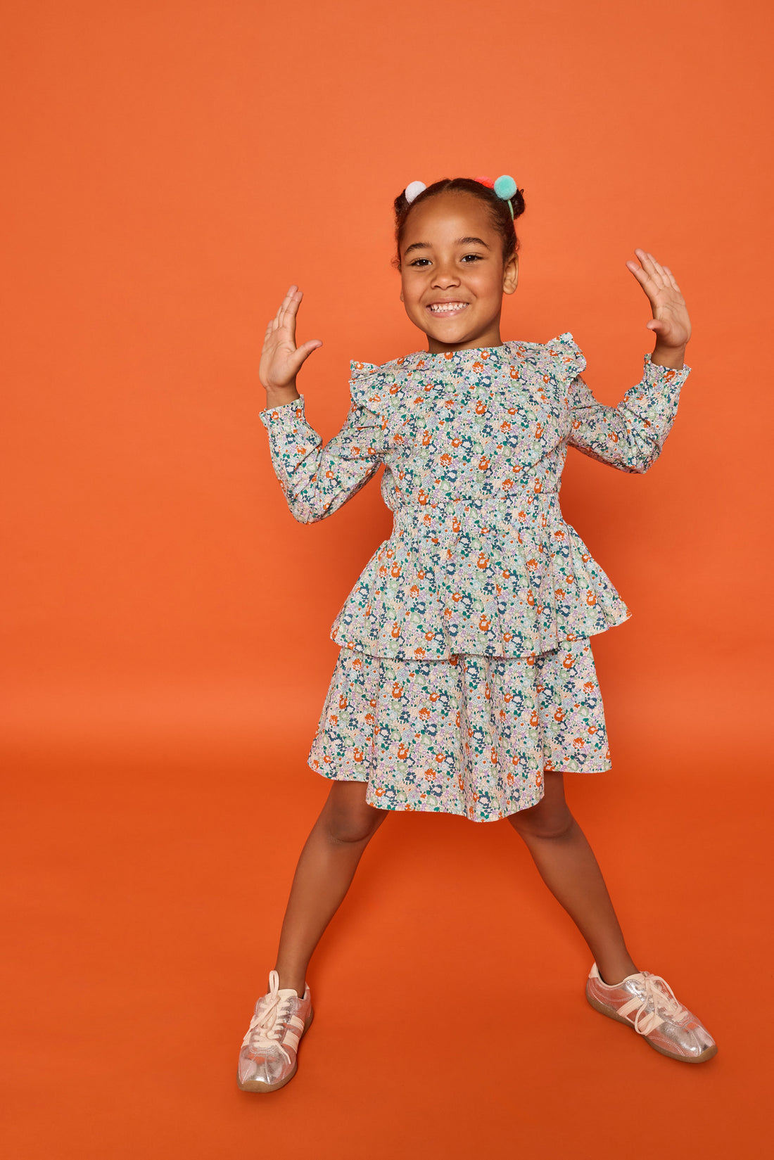 Model can be seen wearing a long sleeve woven dress in an orange/teal/and green floral print. Dress features tiers, elastic ruched waistband, and angel sleeves at the top of the long sleeves for an elevated look. 