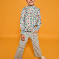 Model can be seen wearing an orange/green/teal floral print woven shirt that features buttons down the front with ruffled detail along neckline and smocking detail at sleeves for an elevated look. Paired back perfectly with our light green pants with elastic waistband and pockets in the front. 
