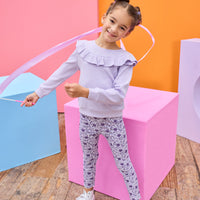 Model can be seen wearing a soft  lilac cable knit long sleeve top that features a ruffle detail cross bust/shoulders for an elevated look. Top pairs back perfectly with knit leggings in a purple floral print to complete the look. 