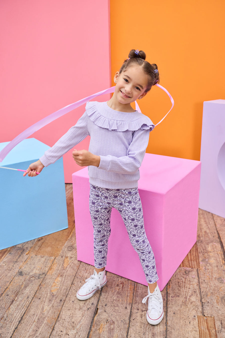 Model can be seen wearing a soft  lilac cable knit long sleeve top that features a ruffle detail cross bust/shoulders for an elevated look. Top pairs back perfectly with knit leggings in a purple floral print to complete the look. 