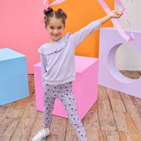 Model can be seen wearing a soft  lilac cable knit long sleeve top that features a ruffle detail cross bust/shoulders for an elevated look. Top pairs back perfectly with knit leggings in a purple floral print to complete the look. 