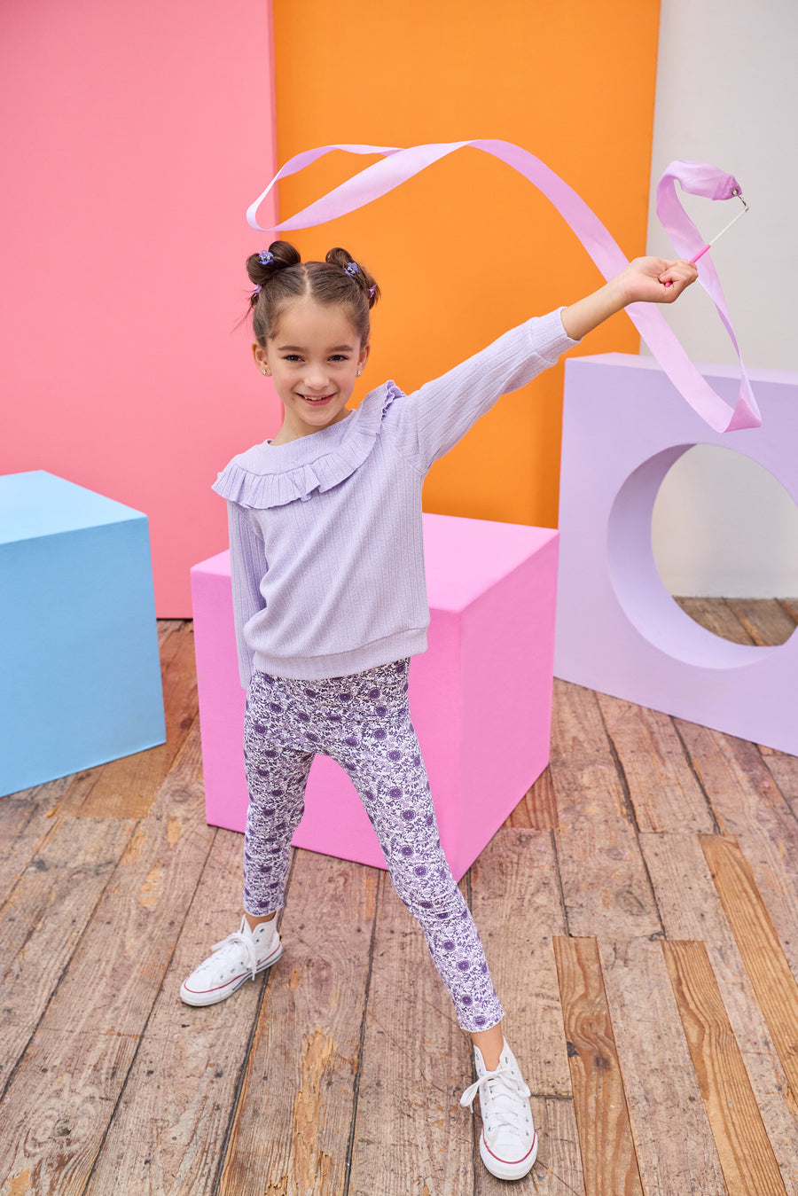 Model can be seen wearing a soft  lilac cable knit long sleeve top that features a ruffle detail cross bust/shoulders for an elevated look. Top pairs back perfectly with knit leggings in a purple floral print to complete the look. 