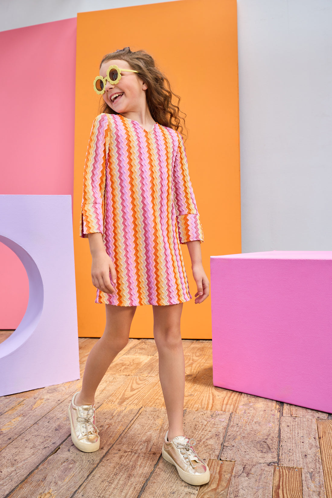 Young girl wearing a colorful striped dress in front of geometrically colored blocks.