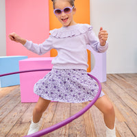 Model can be seen wearing a knit skort in a beautiful purple floral print. Skort features an elastic waistband and built in shorts for a relaxed but secure fit. Top pairs back perfectly with cable knit purple long sleeve top with ruffle detail across bust/top of sleeves to complete the look. 