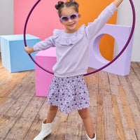 Model can be seen wearing a knit skort in a beautiful purple floral print. Skort features an elastic waistband and built in shorts for a relaxed but secure fit. Top pairs back perfectly with cable knit purple long sleeve top with ruffle detail across bust/top of sleeves to complete the look. 