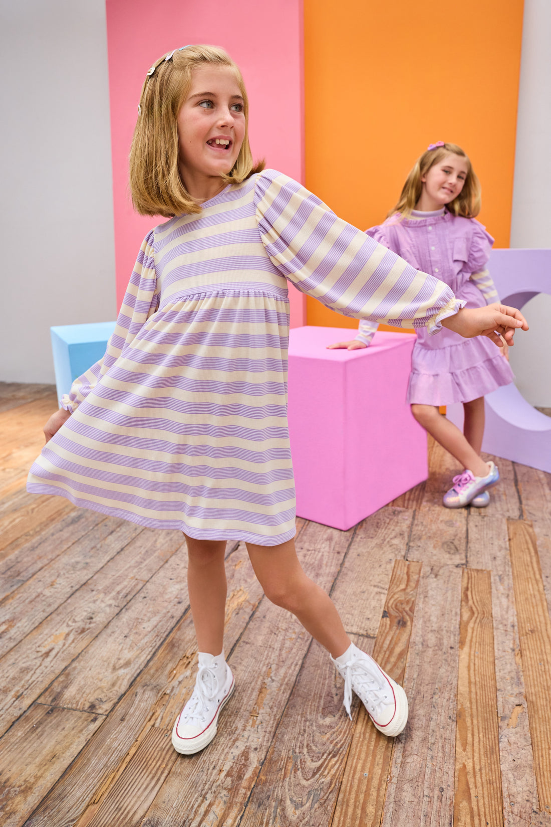 Two young girls in pastel striped dresses standing in a room with colorful walls.