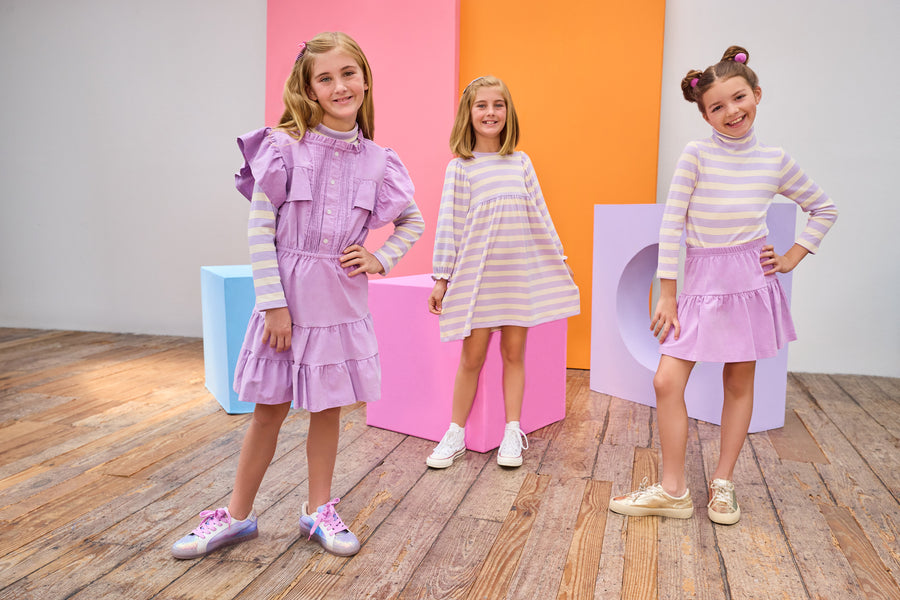 Three young girls in colorful dresses standing in a room with colorful blocks.