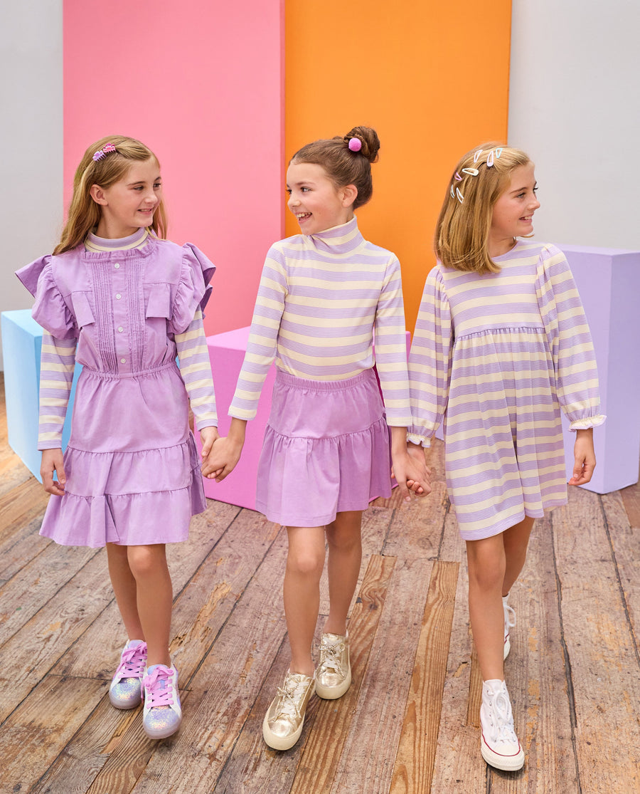 Three young girls holding hands in front of colorful geometric shapes wearing matching outfits.