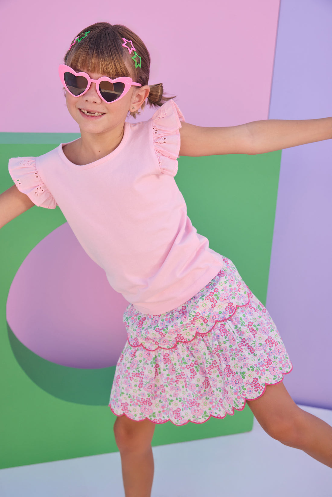 Model can be seen wearing a light pink knit short sleeve top that features eyelet detail on the angel sleeves. Top can be paired back with many bottoms in the line, as it is a solid pink shirt, easy to mix and match. 