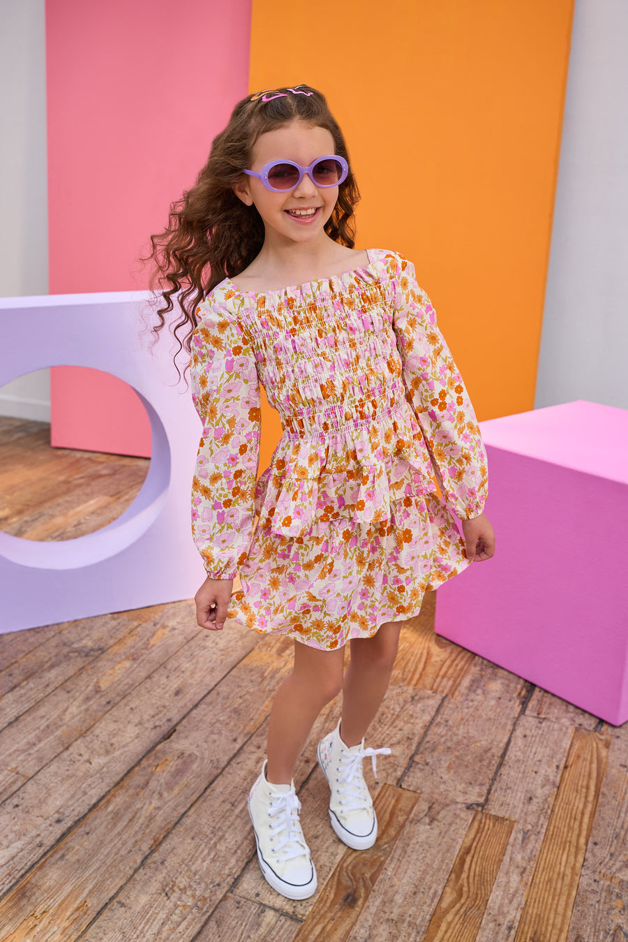 Young girl in a top and skirt standing in front of colorful geometric shapes on a wooden floor.