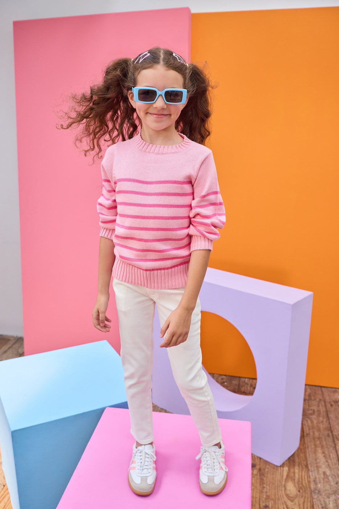 Tween model seen wearing a striped light pink and hot pink sweater paired back with ivory jeans for a comfy yet elevated look. 