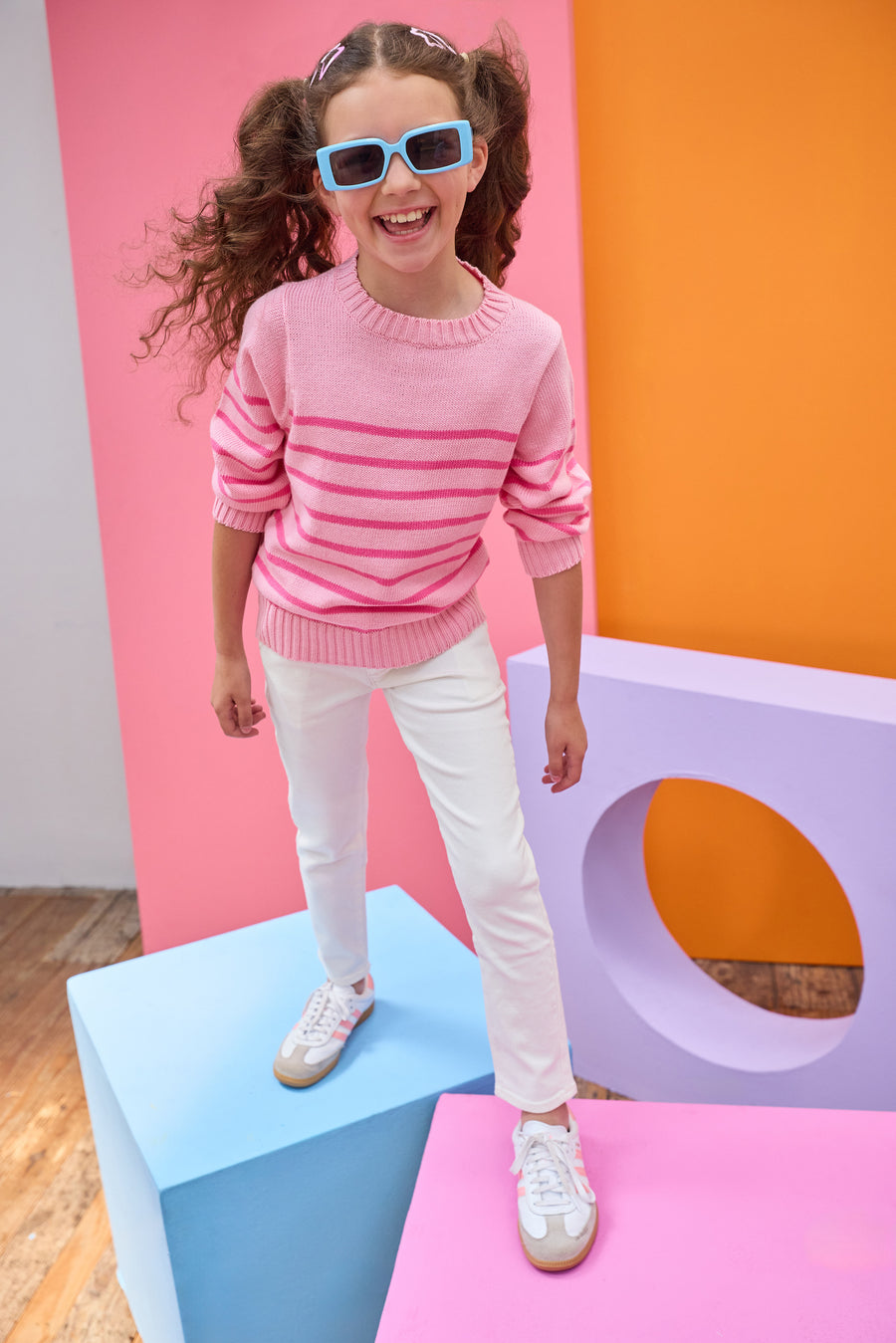 Tween model seen wearing a striped light pink and hot pink sweater paired back with ivory jeans for a comfy yet elevated look. 