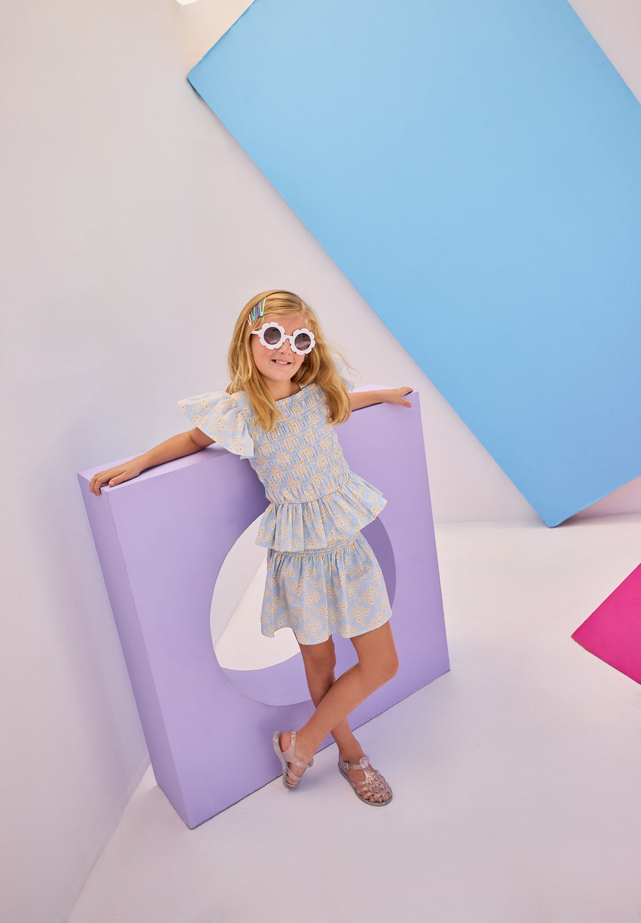 Model can be seen wearing gorgeous woven top that has a ruching feature across middle of top. Top is made of yellow and white flowers printed on a light blue background and also features angel sleeves to complete the look. Paired back perfectly with our shirred circle skirt in the same print for a complete set. 