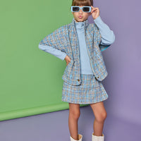 Model can be seen wearing a tweed cape in a blue tweed pattern. Cape pairs back with the matching tweed skort and ribbed turtleneck underneath to complete the look.